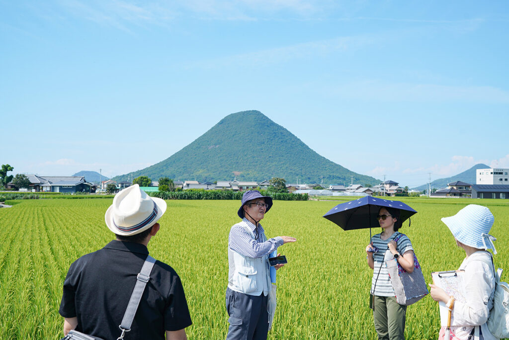 講義の後、宇多津を流れる大束川（だいそくがわ）から上流に8kmほど、香川県丸亀市下法軍寺（しもほうぐんじ）あたりにきました。向こうに見えるのは、讃岐富士こと飯野山（いいのやま / 標高：422m）です。